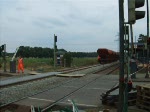 Die Lok V2.023 der AKN schiebt am 18.06.08 ein fnf Schotterwaggons mit Signalhorn ber den Bahnbergang Meeschensee in Henstedt-Ulzburg . 